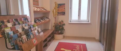 A hotel reception area with a red carpet, a display of brochures, a potted plant, and a window with a view.