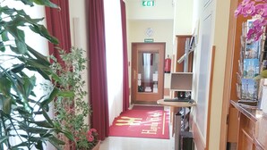 Eine Hotelhalle mit rotem Teppich, Topfpflanzen, einer Rezeption und einer Uhr an der Wand.