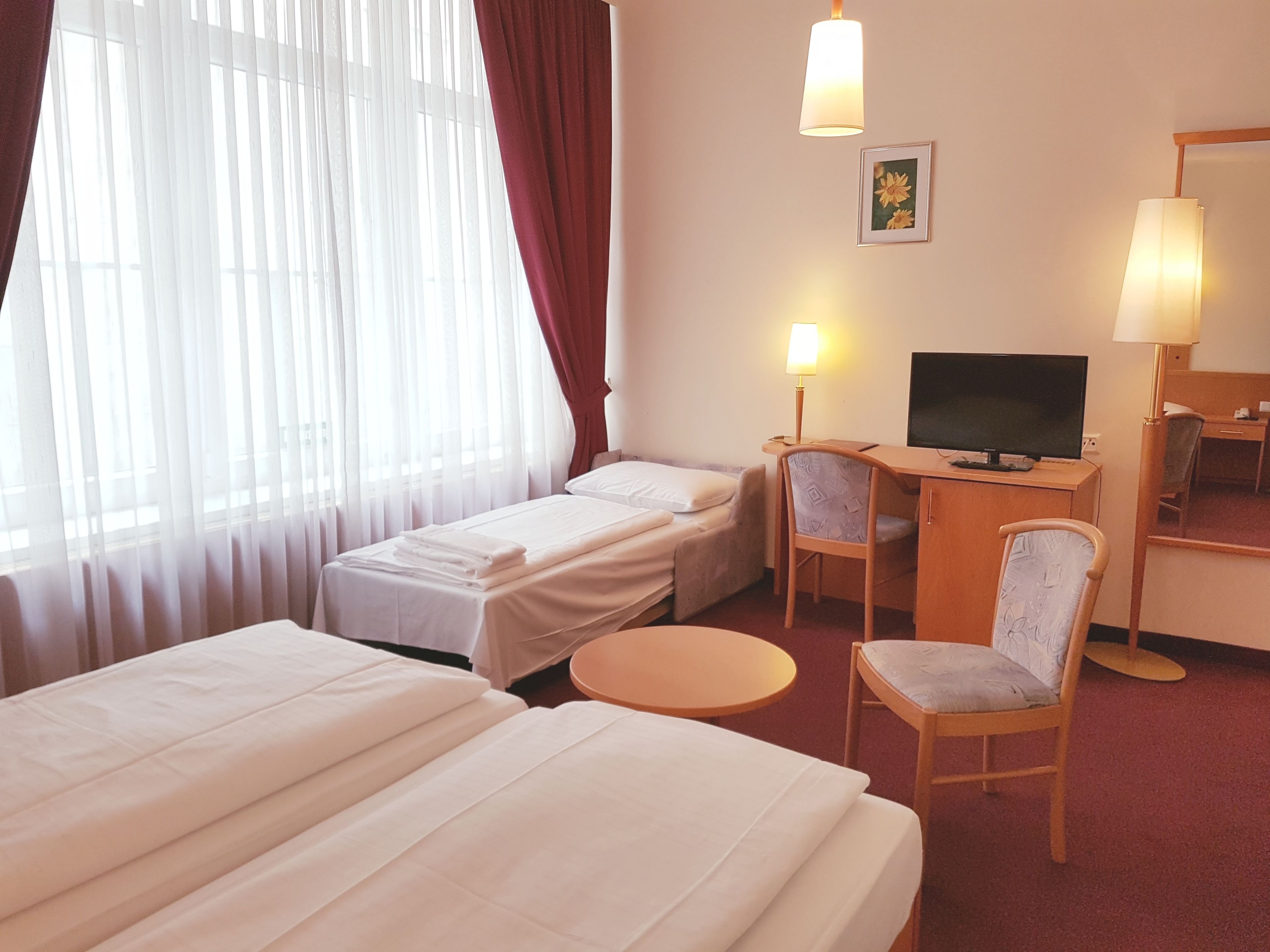 Habitació d'hotel amb dos llits, un escriptori amb televisió, una cadira i una taula petita.