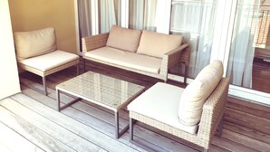 Ein Balkon mit Korbmöbeln, darunter eine Couch und zwei Stühle, sowie ein kleiner Tisch.