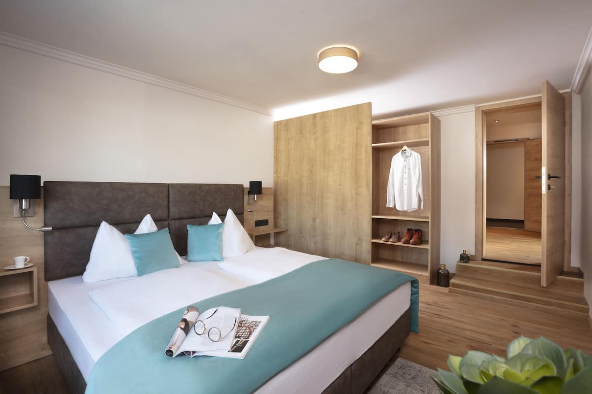 Ein modernes Hotelzimmer mit einem großen Bett, einem Holzkopfschild und einem eingebauten Kleiderschrank mit Regalen.
