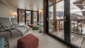 Ein moderner Lounge-Bereich mit Sitzgelegenheiten, einer Lampe und großen Fenstern mit Blick auf die Berge.