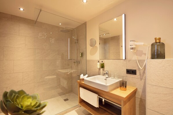 Un baño moderno con ducha envuelta en vidrio, tocador de madera con lavamanos y un espejo grande.