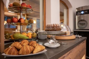 A breakfast buffet with croissants, fruits, and a cake on display.