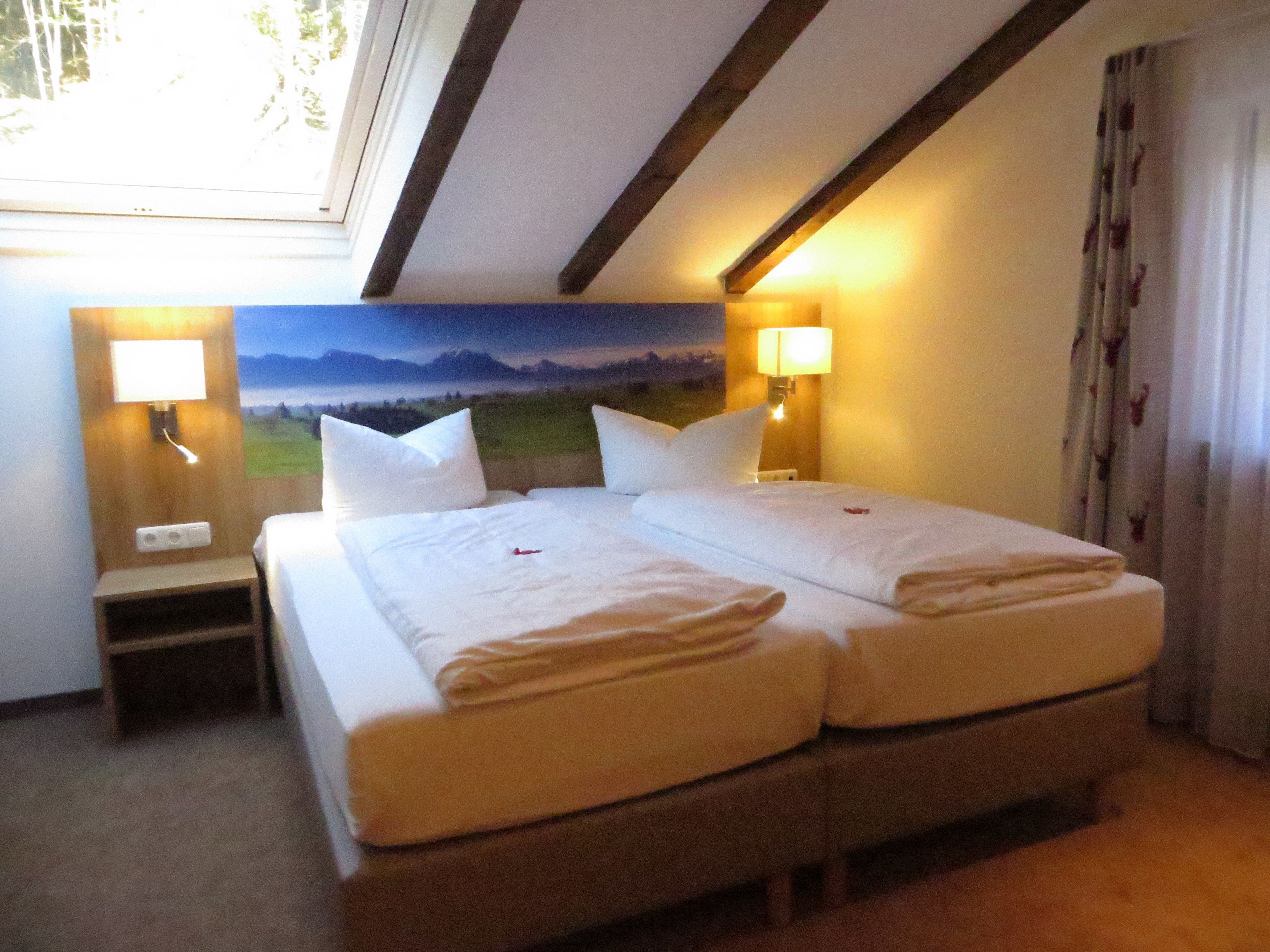 A double bed with two pillows, a nightstand, a lamp, and a painting of a landscape on the wall.