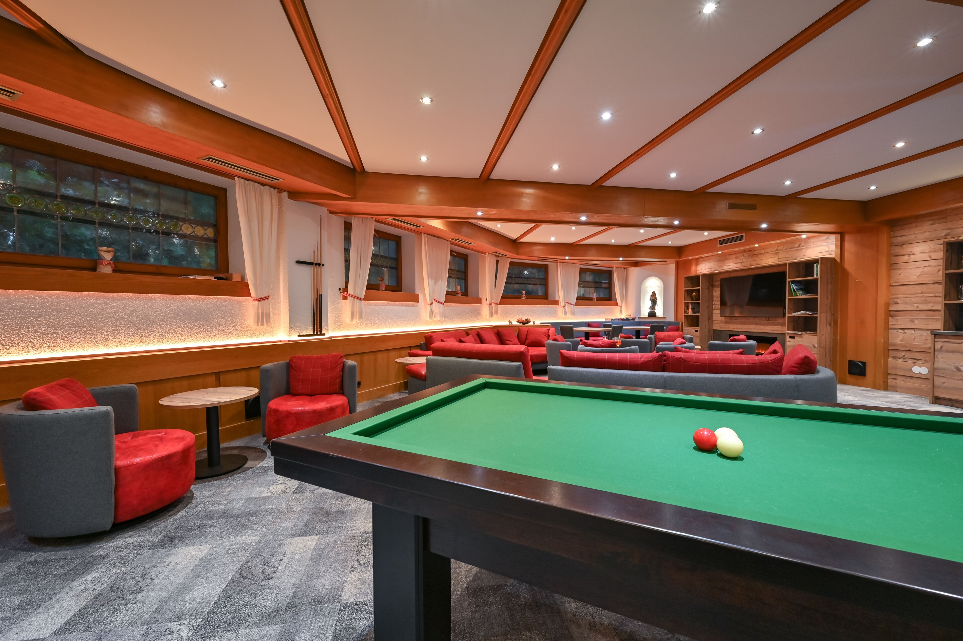 A pool table with red and grey chairs, a bar area, and a seating area with red sofas.