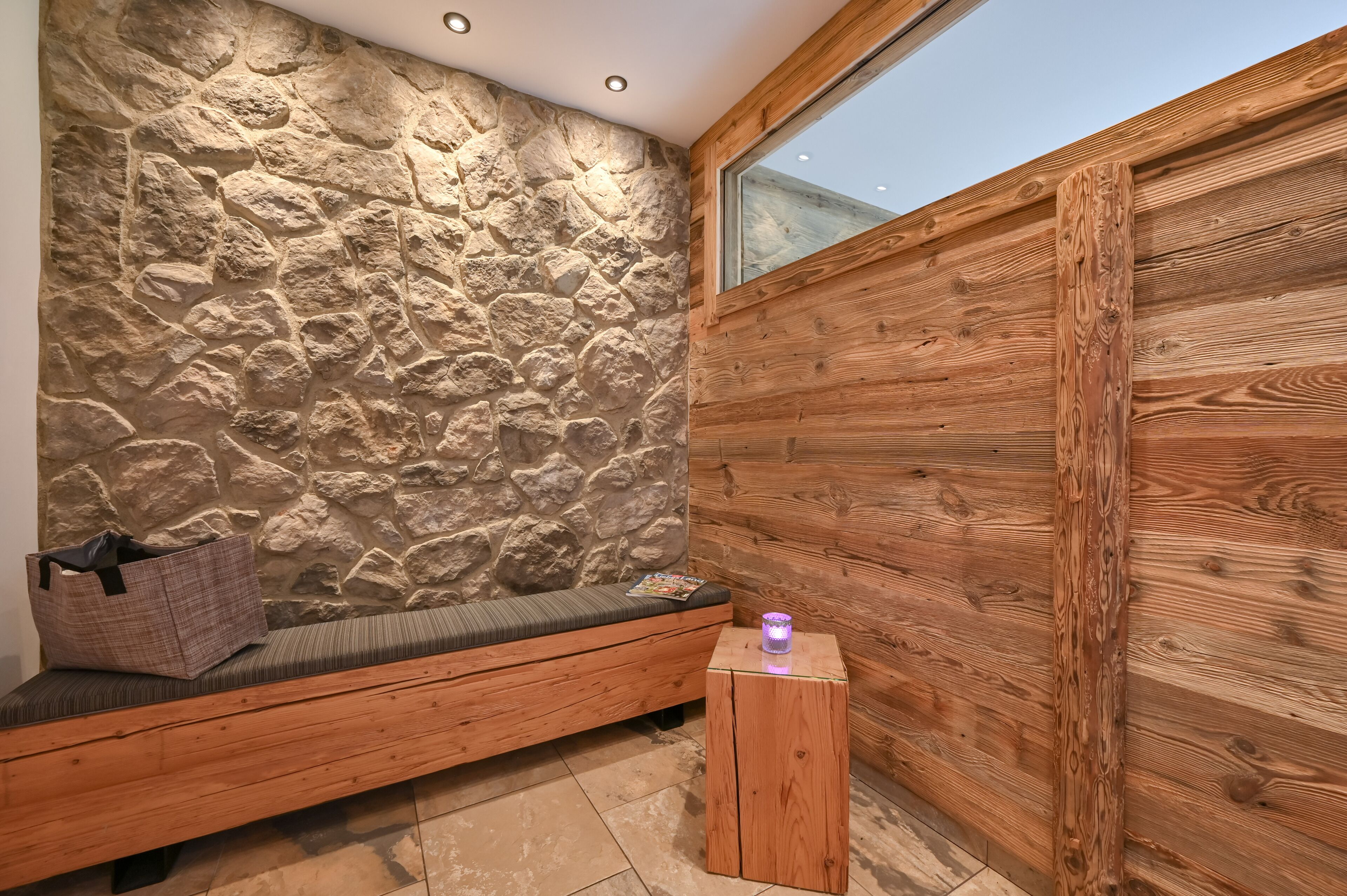 A room with a stone wall, wooden bench, and a small wooden stool.
