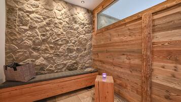 A room with a stone wall, wooden bench, and a small wooden stool.