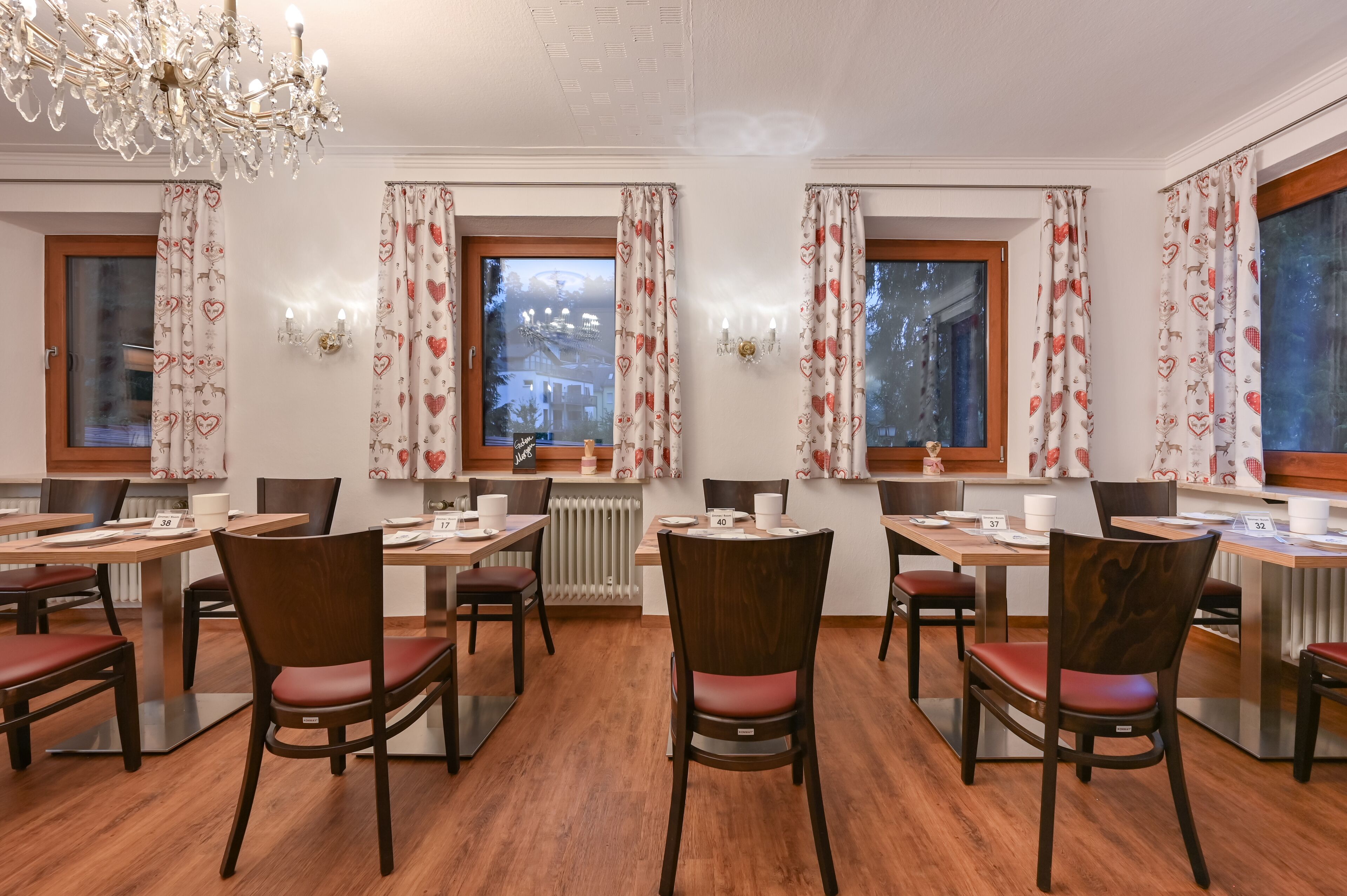A dining area with multiple tables and chairs, heart-patterned curtains, and a chandelier.