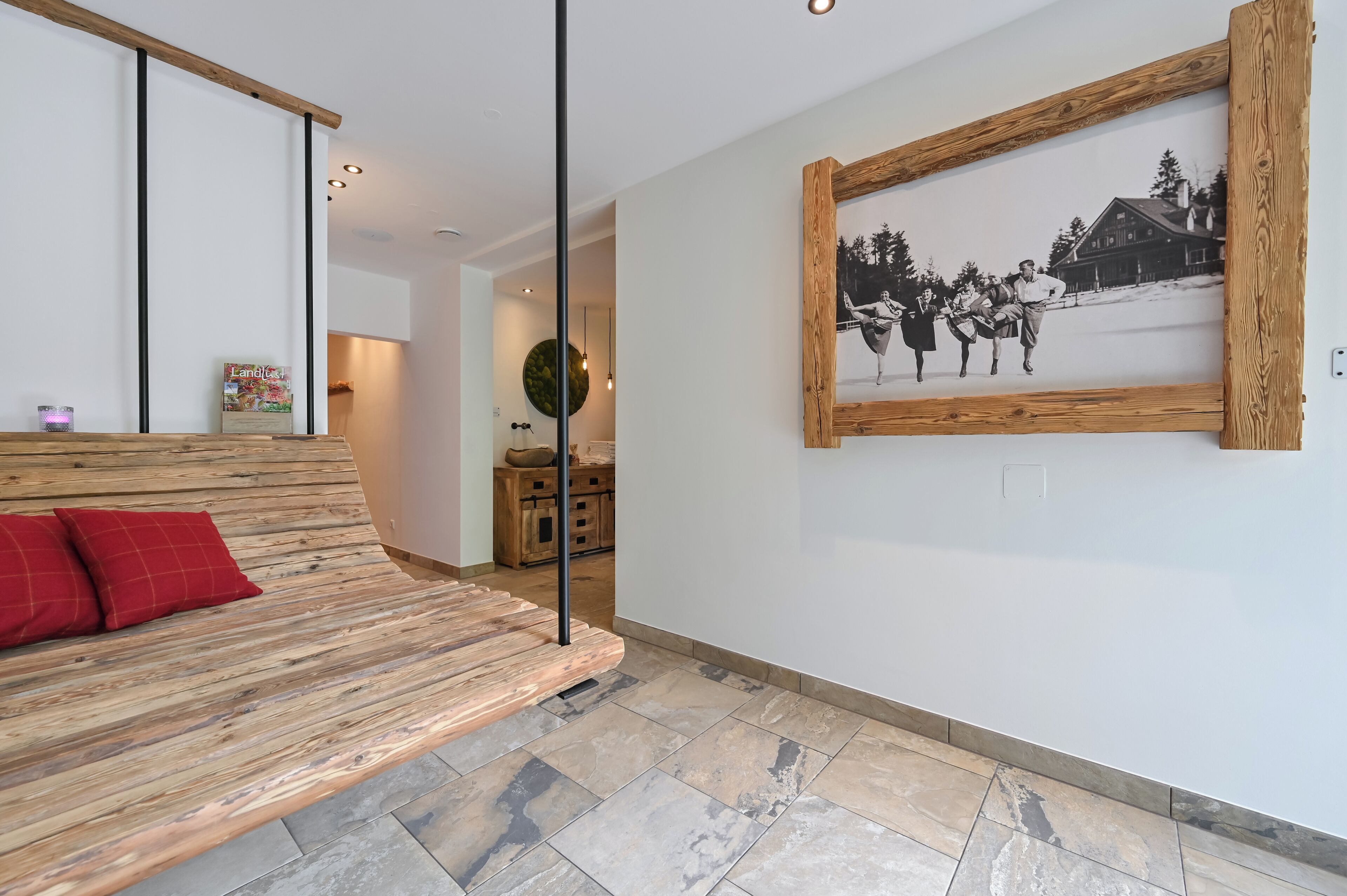 Un interior moderno con un banco de madera, una fotografía blanco y negro enmarcada en la pared y una cocina al fondo.