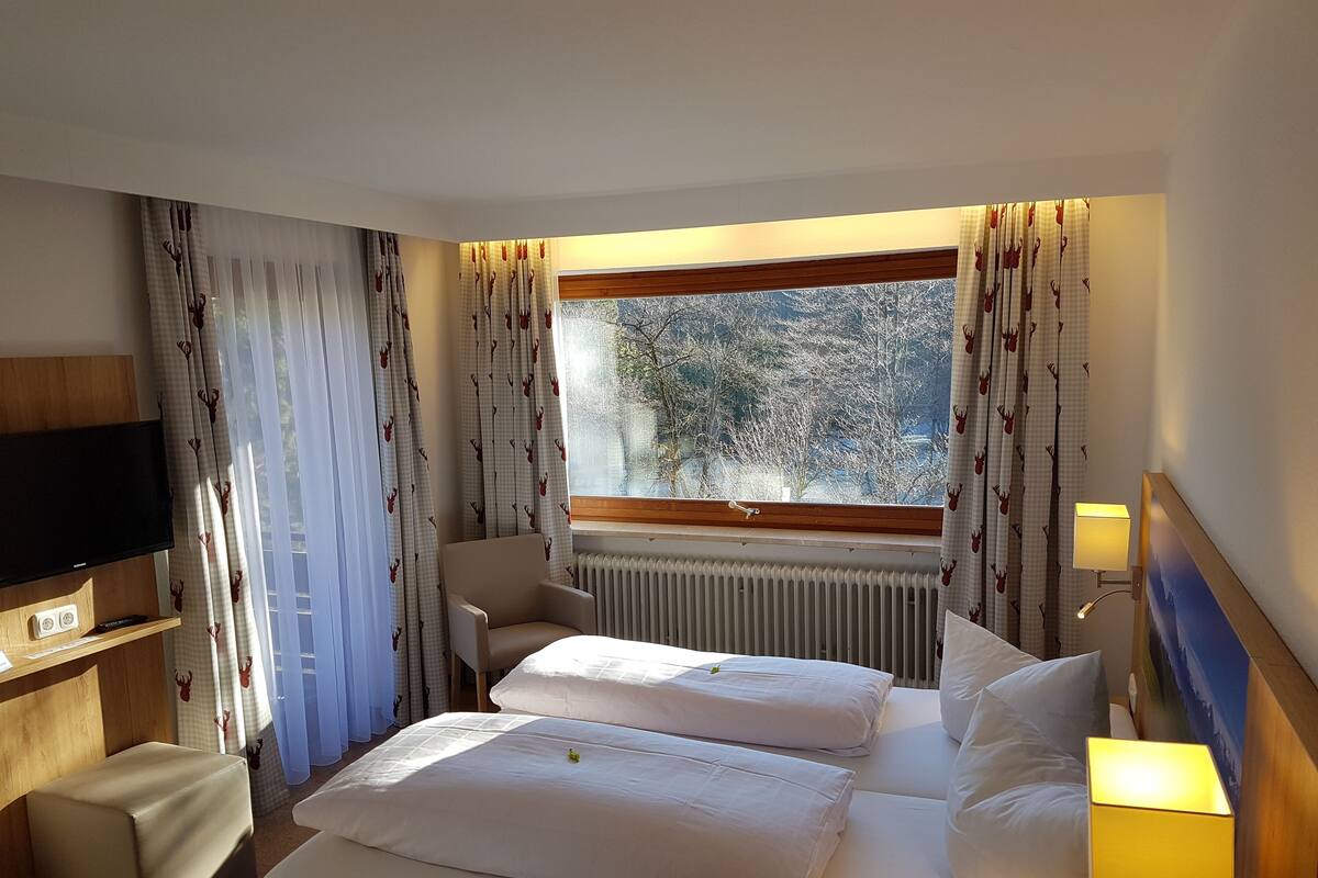 A hotel room with a bed, a TV, a lamp, and a window with curtains.