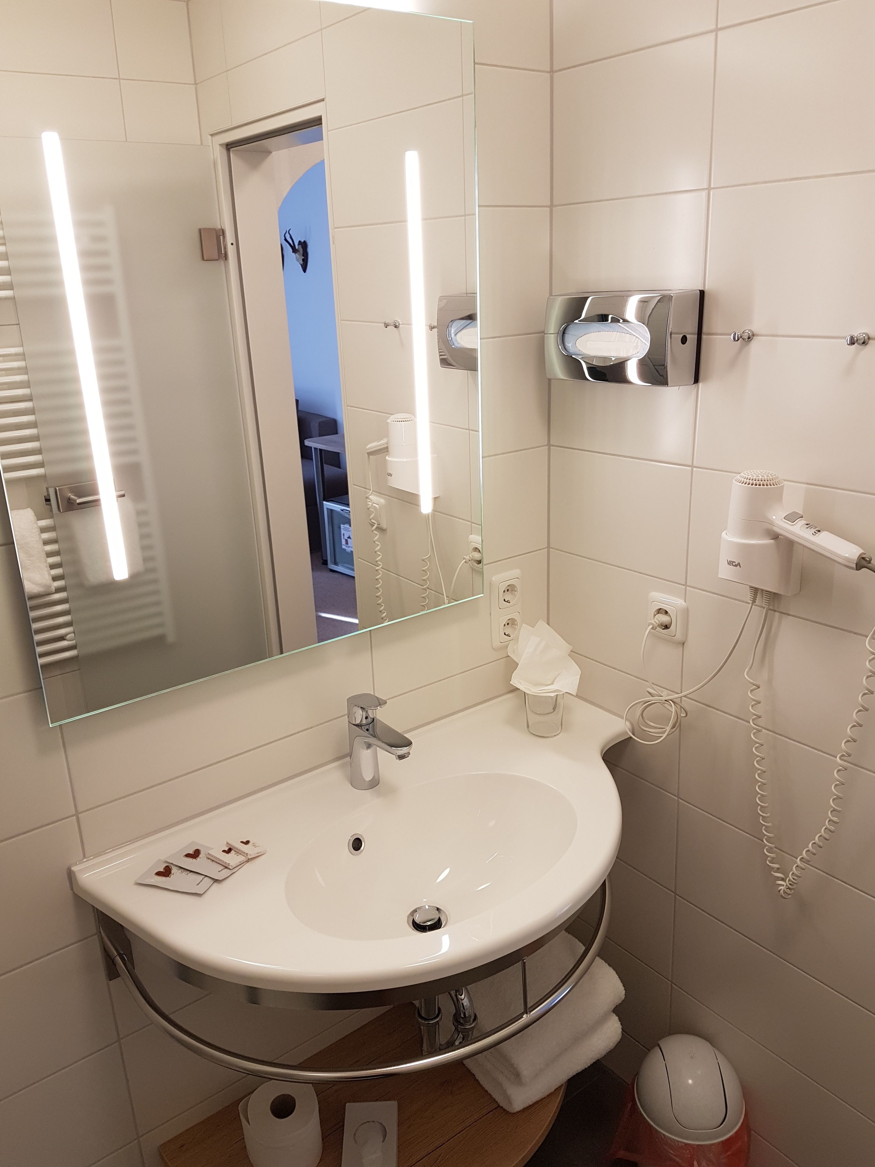 A modern bathroom with a white sink, a mirror, a hairdryer, and a towel rack.