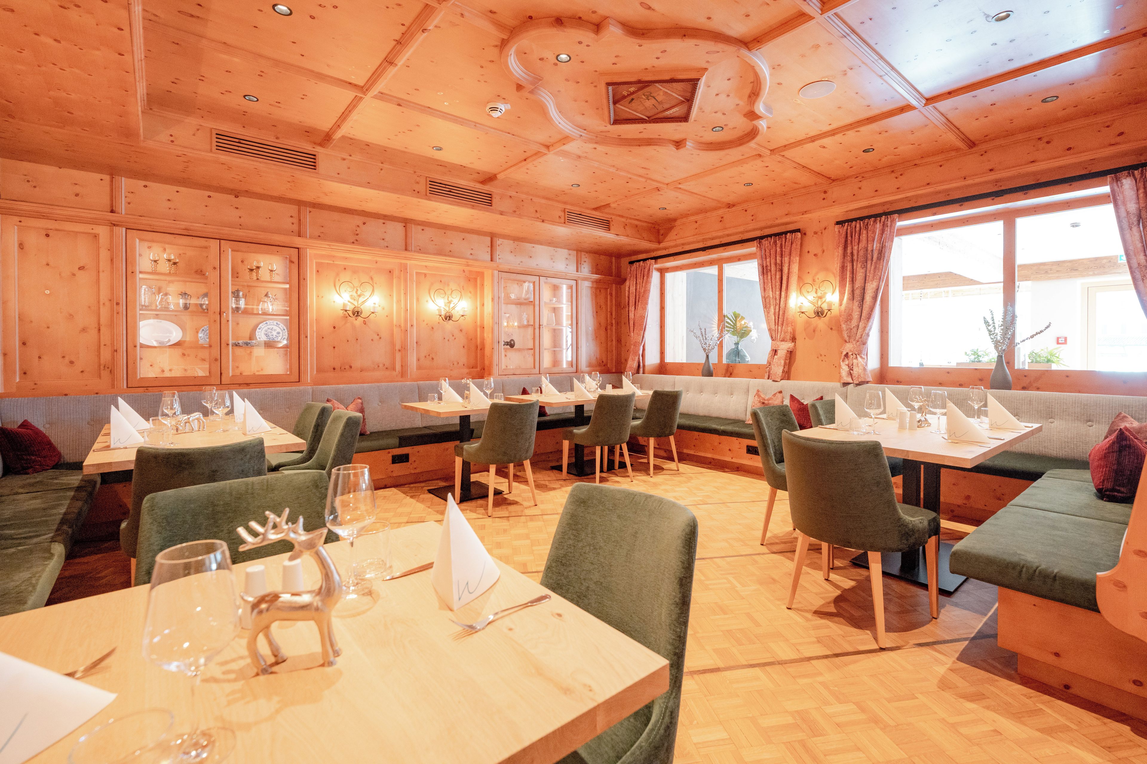 A restaurant with wooden paneling, green upholstered seating, and a high ceiling with recessed lighting.