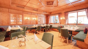 A restaurant with wooden paneling, green upholstered seating, and a high ceiling with recessed lighting.
