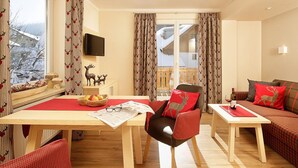 A cozy living room with a wooden dining table, a sofa, and a TV mounted on the wall. - Vital Hotel Wiedemann (Fuessen)