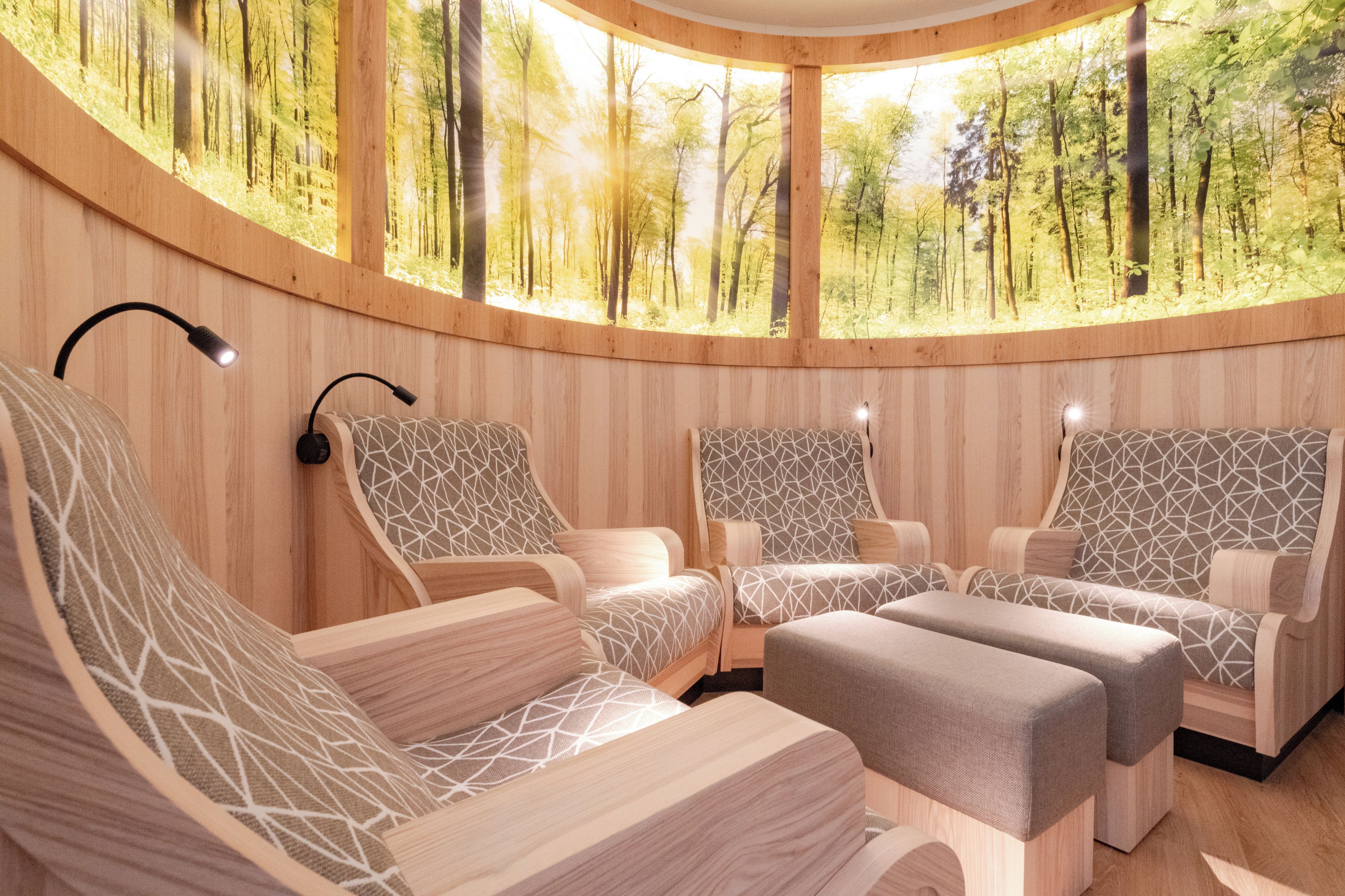 Ein rundes Zimmer mit Holzwänden und Blick auf einen Wald. Vier Stühle mit geometrischen Mustern und ein kleiner Tisch sind ebenfalls vorhanden.