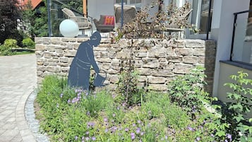 Eine steine Mauer mit einem Garten davor, inklusive violetten Blumen und einem kleinen Baum.