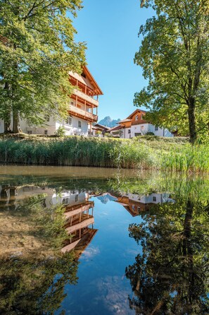 Ein traditionelles Chalet mit Holzbalkon, Spiegelung im Wasser und Bergkulisse.