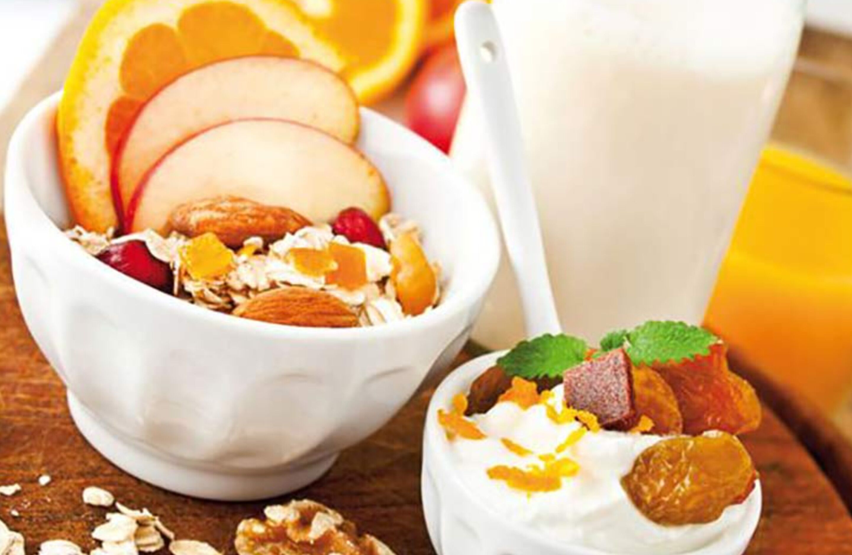A bowl of cereal with fruits and nuts, a glass of milk, and a spoon.