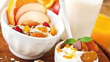 A bowl of cereal with fruits and nuts, a glass of milk, and a spoon.