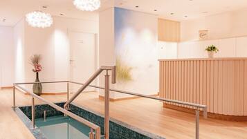 Un moderno vestíbulo de hotel con mostrador de recepción, zona de espera, piscina con barrera de cristal y escalera que conduce al piso superior.
