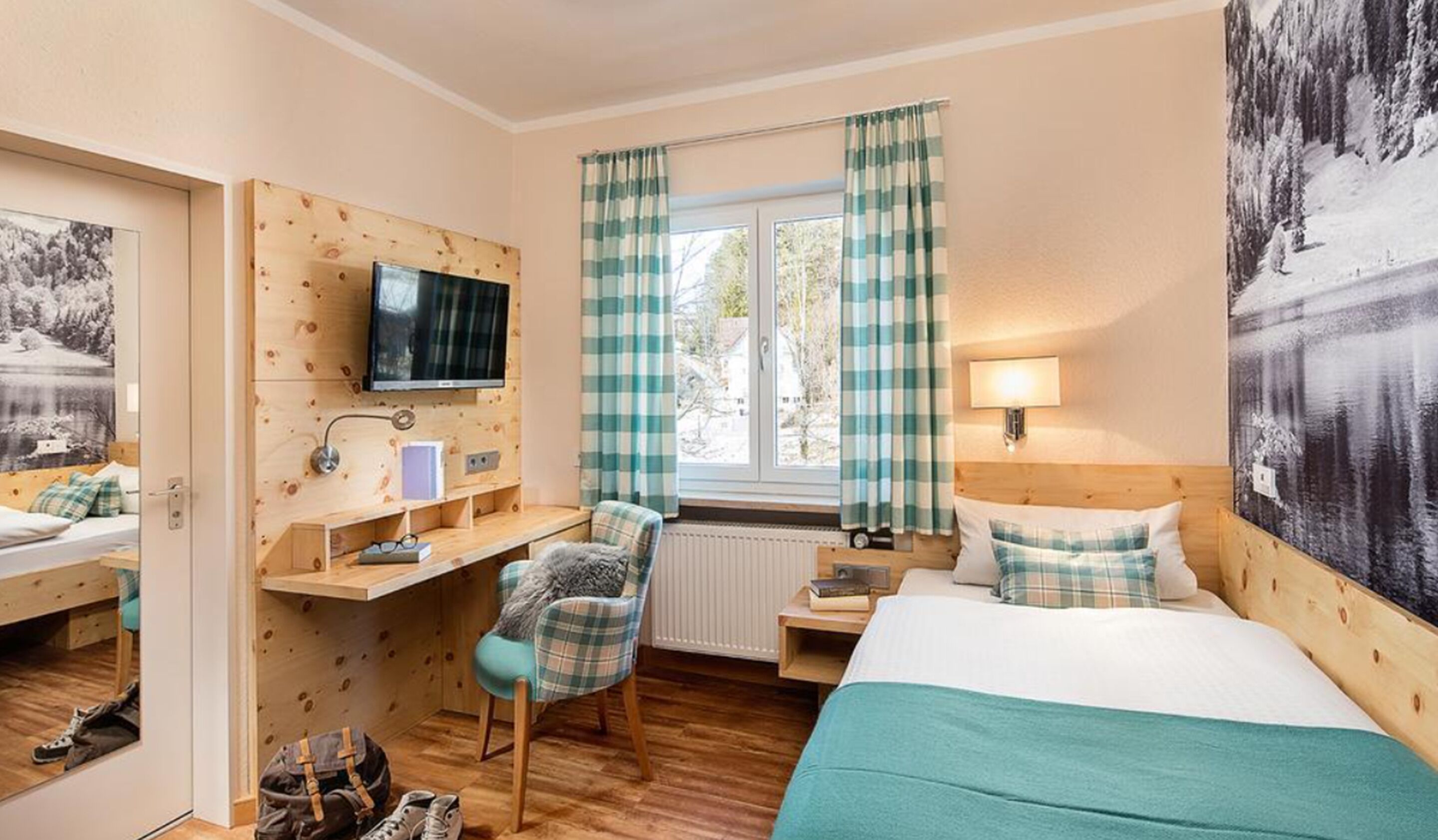 Una habitación de hotel con un escritorio de madera, una cama, una silla, un televisor y una ventana con cortinas.