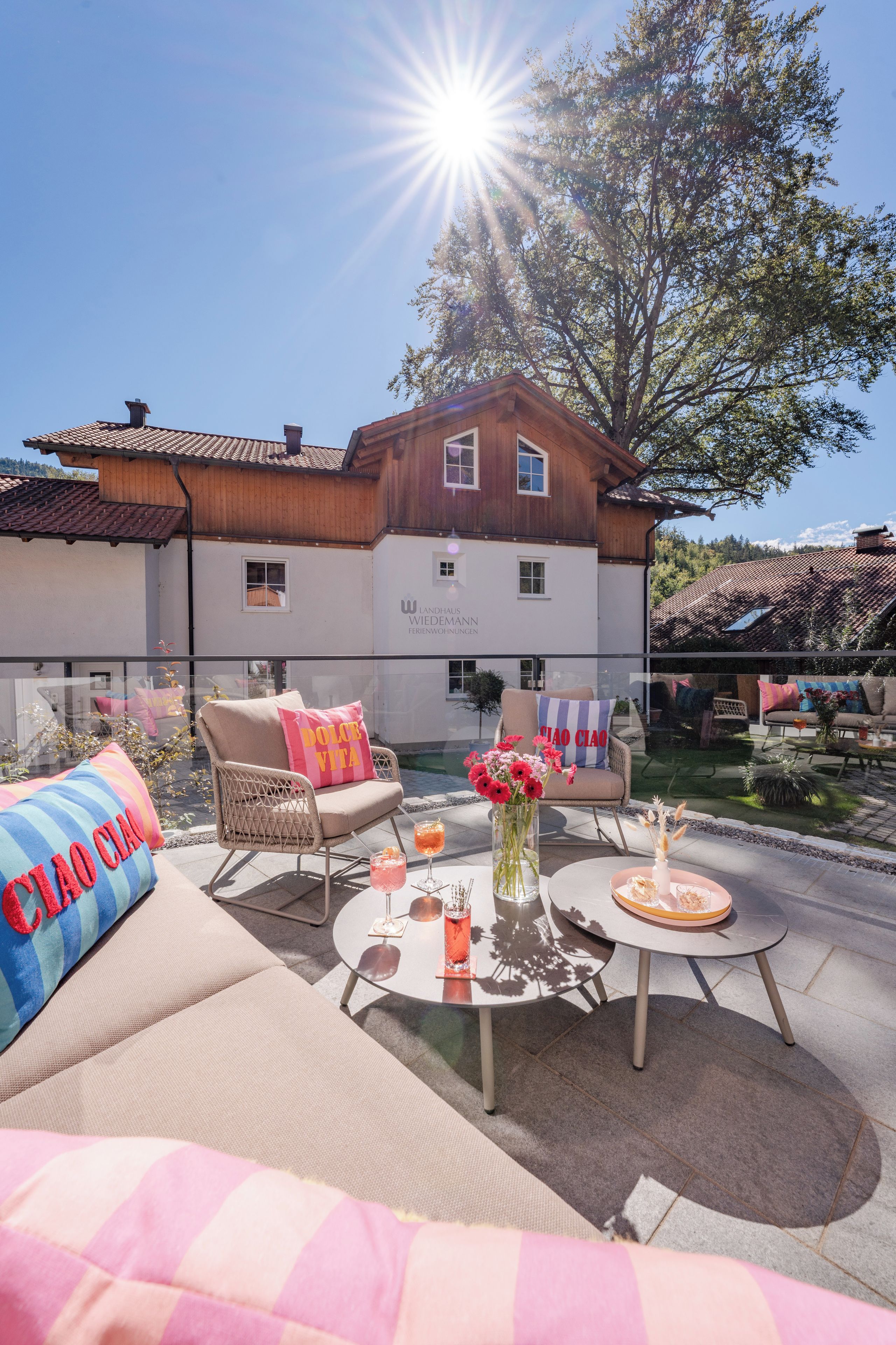 A sunny outdoor seating area with a pool, a wooden building in the background, and a clear sky.