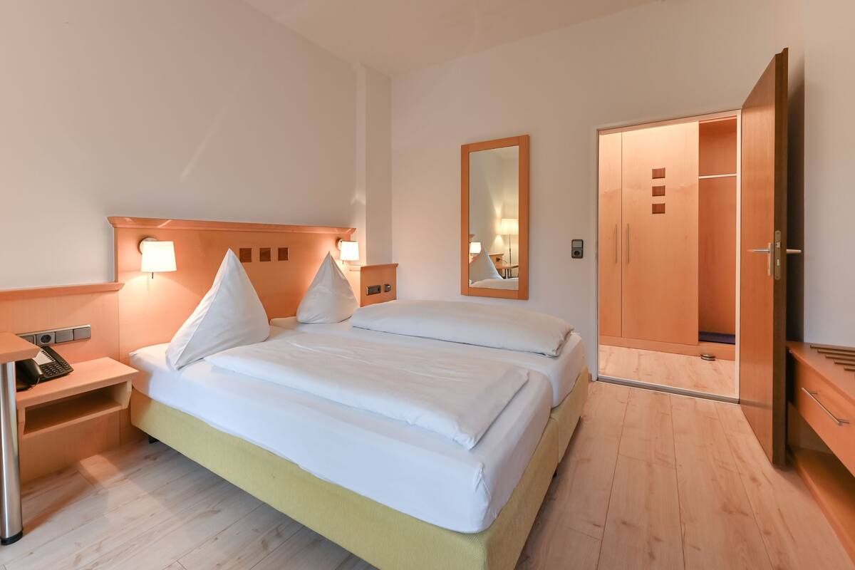 A hotel room with a bed, bedside tables, a wardrobe, and a mirror.
