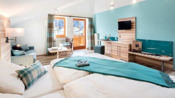 A modern hotel room with a large bed, a desk, a chair, a TV, and a view of the outdoors. - Vital Hotel Wiedemann (Fuessen)