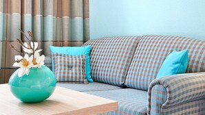 A room with a checkered sofa, a teal vase with flowers, and a wooden table. - Vital Hotel Wiedemann (Fuessen)