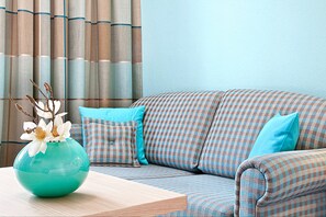 Una habitación con un sofá a cuadros, un florero verde azulado y una mesa de madera.