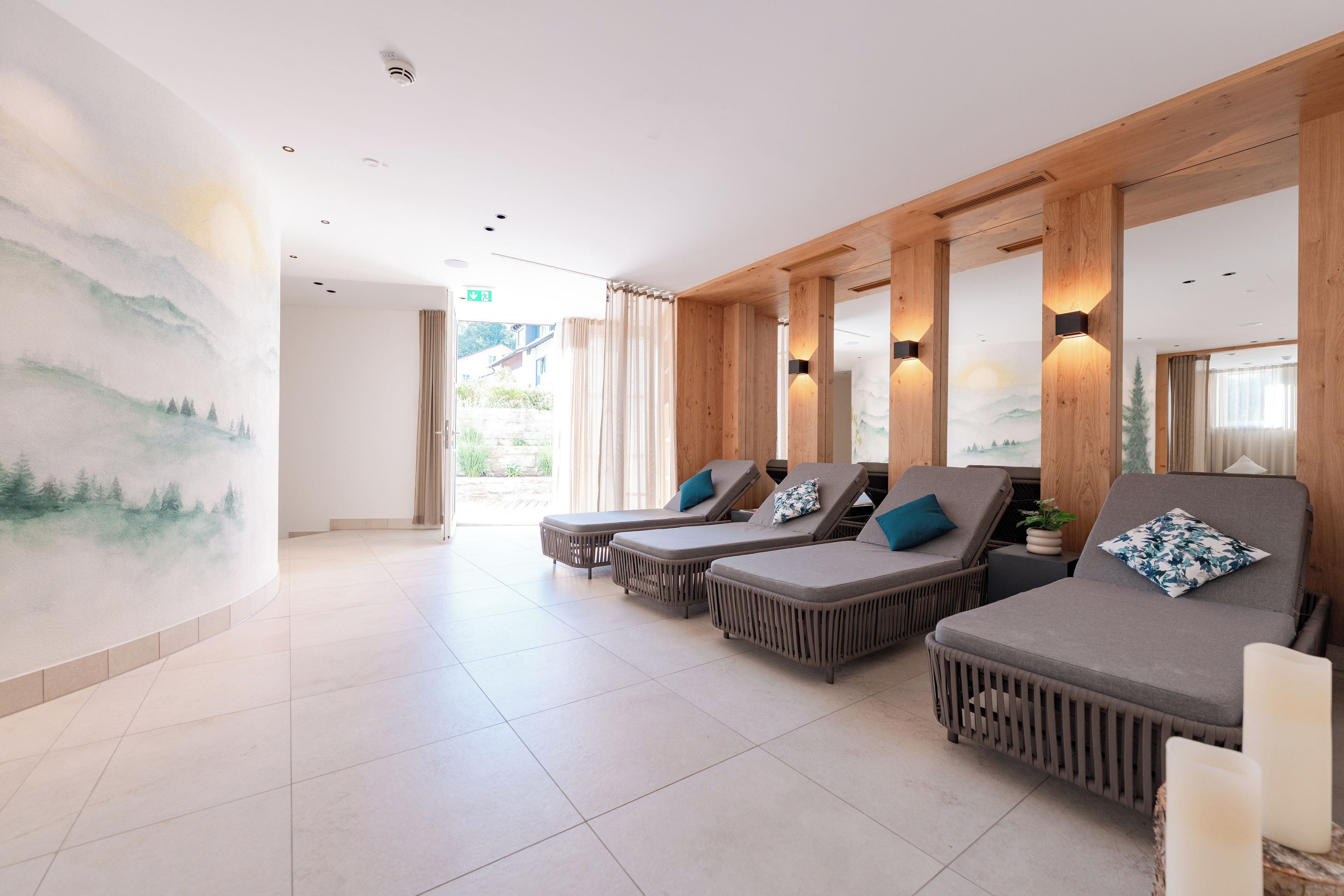 A spa area with three loungers, a large mural, and a view of the outdoors.