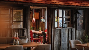 A rustic wooden interior with a wooden table and chairs, a window with a view, and hanging light fixtures. - Hotel Bergruh (Fuessen)