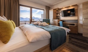 A modern hotel room with a large bed, a TV mounted on the wall, and a view of mountains through the window. - Hotel Bergruh (Fuessen)