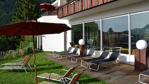 A modern outdoor lounge area with sun loungers and a red umbrella, overlooking a mountainous landscape. - Hotel Bergruh (Fuessen)