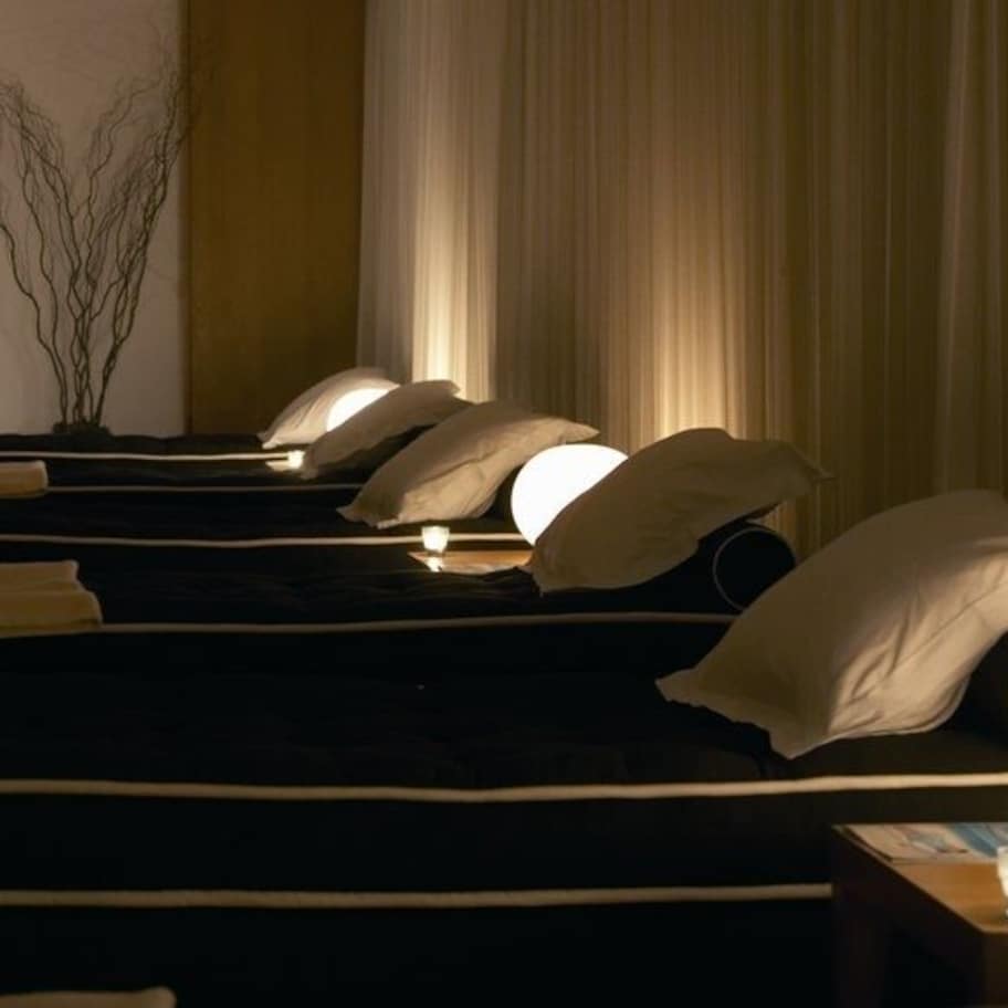 A hotel room with multiple beds, each with a pillow and a bedside lamp.