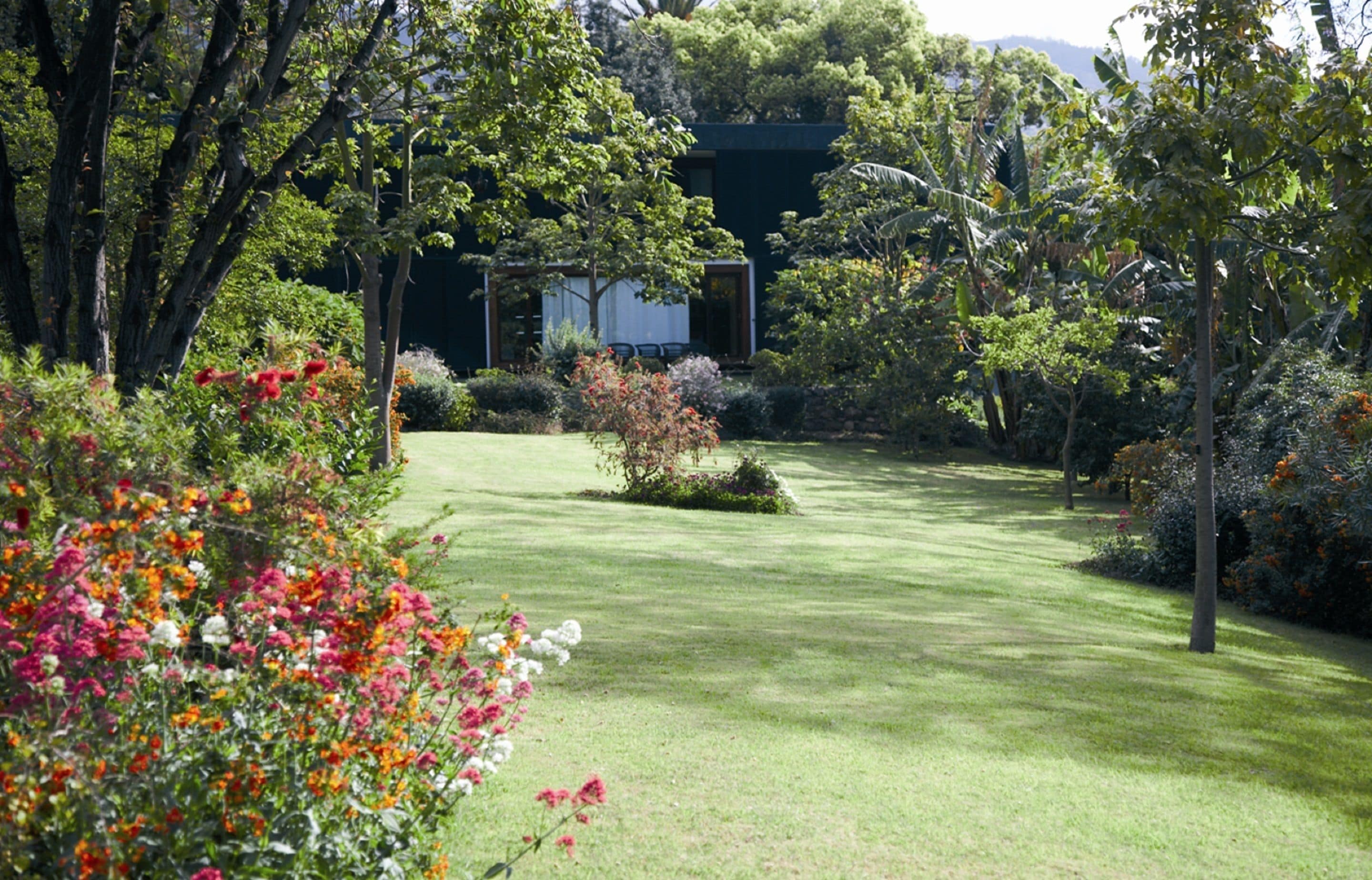 A well-maintained garden with a variety of flowering plants and trees, a neatly trimmed lawn, and a building in the background.