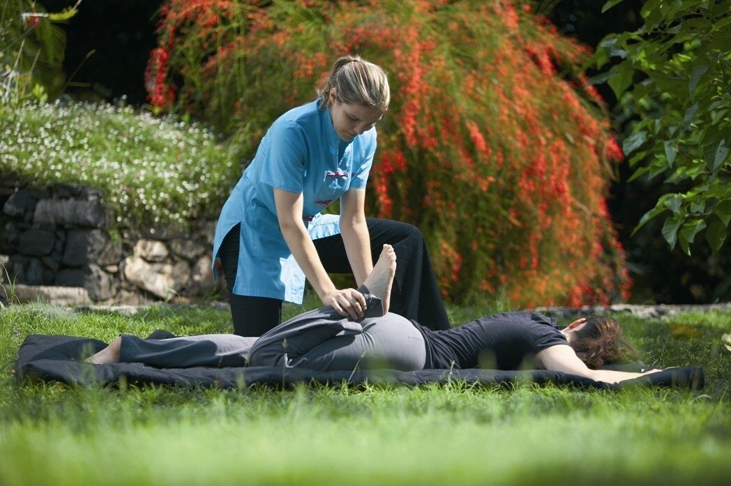 A person lying on a mat outdoors with another person assisting them.
