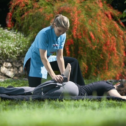 A person lying on a mat outdoors with another person assisting them.