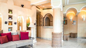 A lobby with a sofa, wicker furniture, and wall-mounted lights. - Villa Royale Montsouris (Paris)