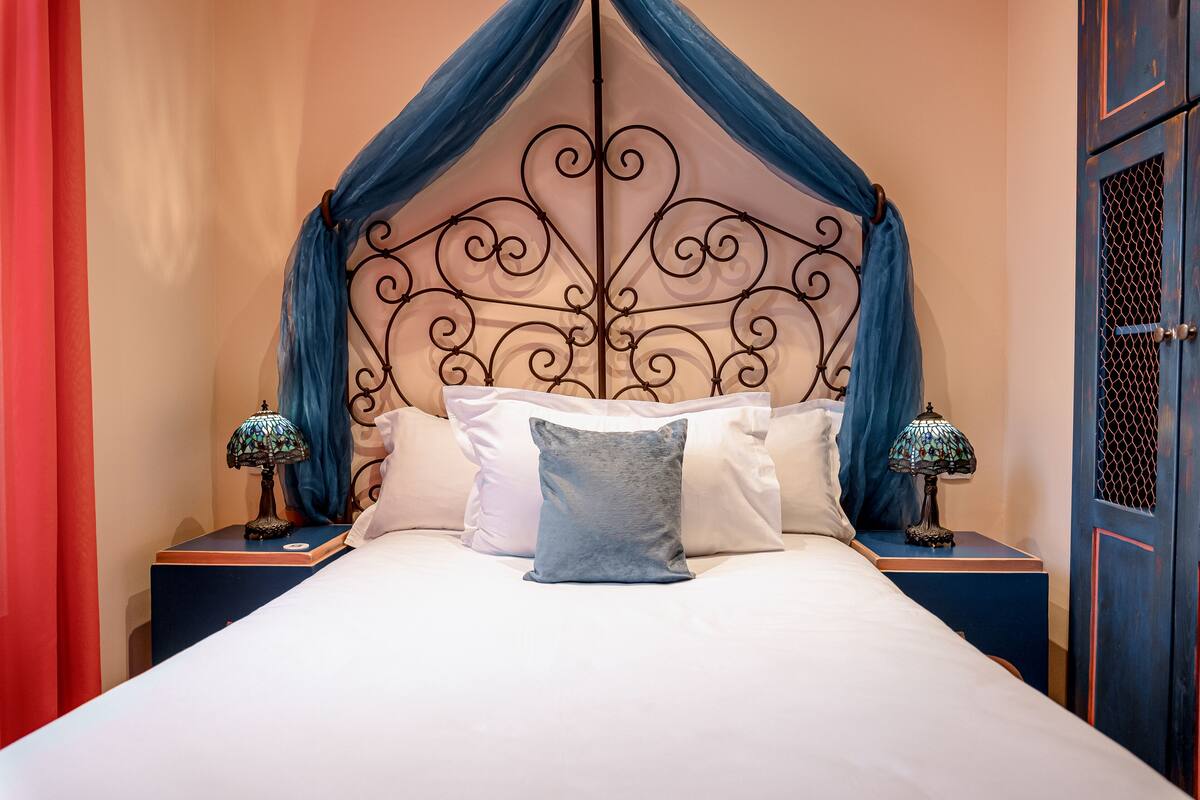 A bed with a decorative metal headboard, two bedside tables with lamps, and a red curtain on the left.