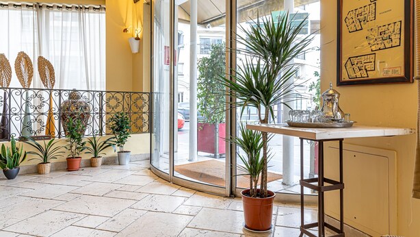 A hotel lobby with a tiled floor, potted plants, a glass door entrance, and a framed map on the wall. - Villa Royale Montsouris (Paris)