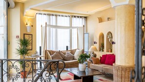 A spacious living room with a large sofa, a coffee table, and a potted plant. There is a staircase with a wrought iron railing leading to an upper level. - Villa Royale Montsouris (Paris)