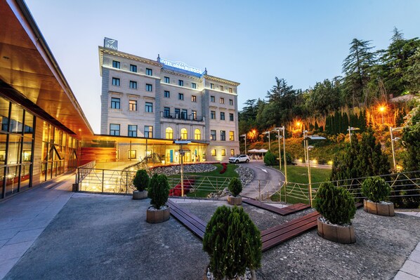 Un hotel con fachada moderna, un patio ajardinado y una zona de estacionamiento.