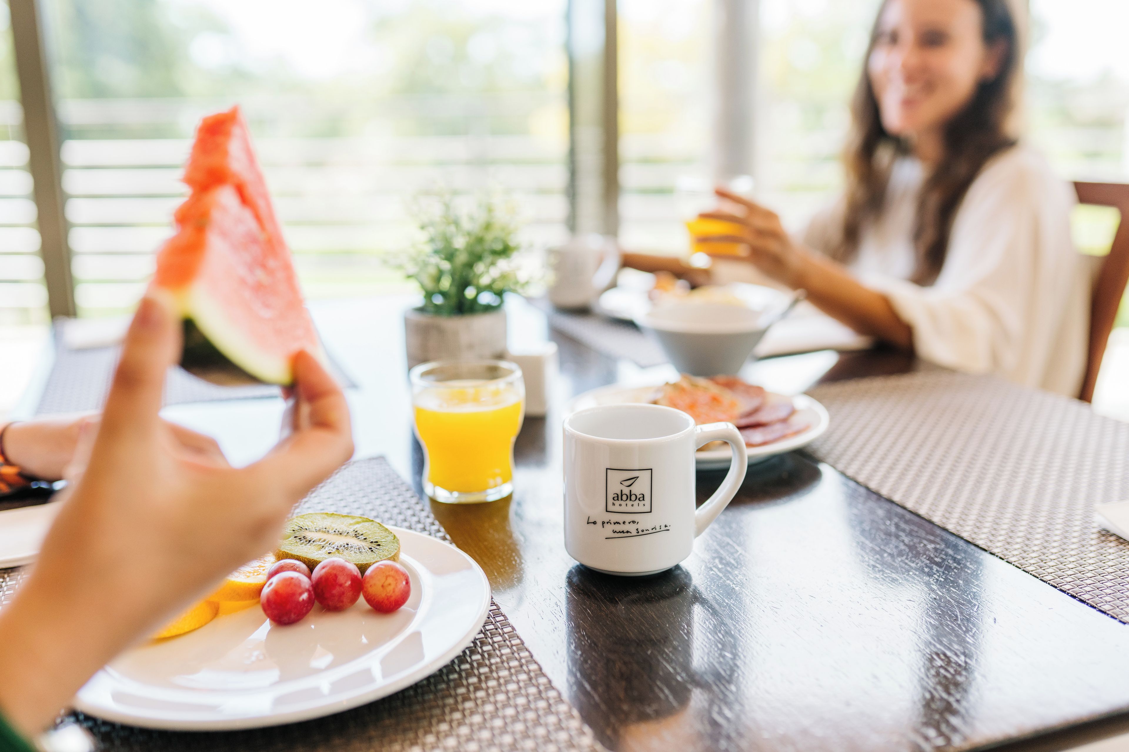 Un desayuno con una fuente de fruta, un vaso de jugo de naranja y una taza de café sobre una mesa.
