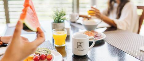 Un desayuno con una fuente de fruta, un vaso de jugo de naranja y una taza de café sobre una mesa.