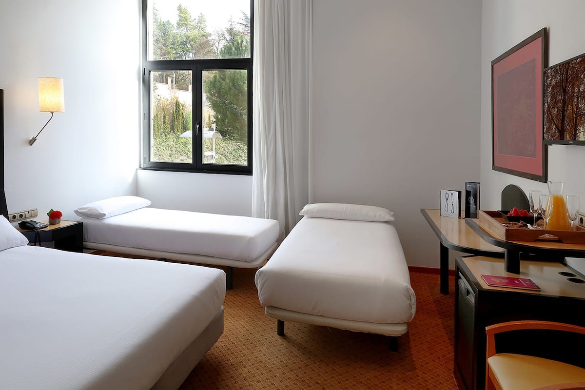 Habitació d'hotel amb dos llits, escriptori, cadira, finestra amb vistes i làmpada.
