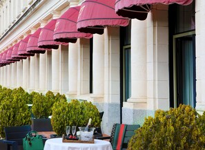 Een rij terras tafels met parasols, een groene handtas en een champagnefles op een dienblad.