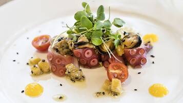 Un plato blanco con tentáculos de pulpo, tomates cherry y microgreens.