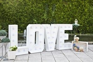 Store hvide bogstaver, der staves "LOVE", med knopper, foran et grønt baggrund og en sø.